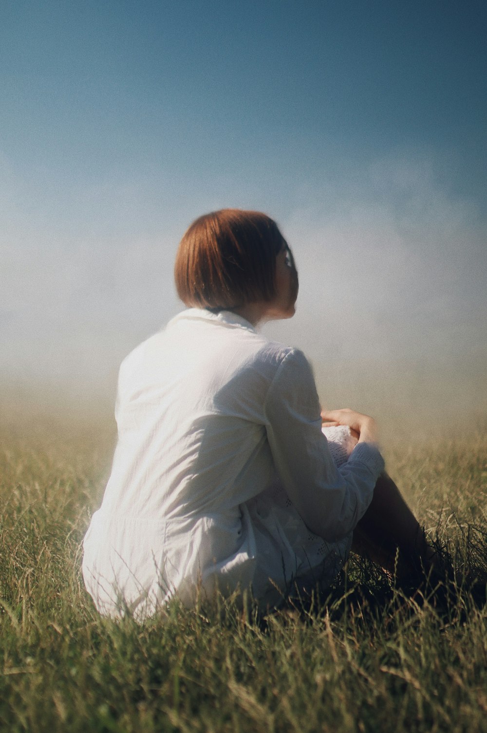 woman in white long sleeve shirt sitting on green grass field during daytime