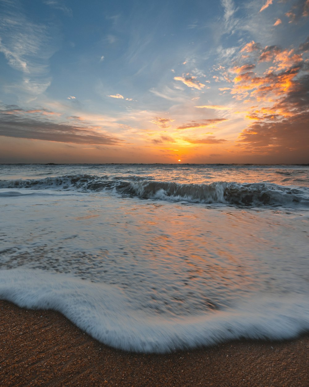 ocean waves crashing on shore during sunset