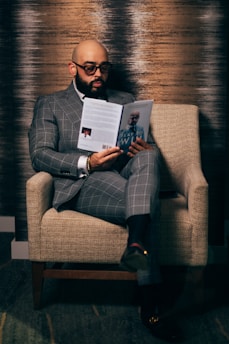 man in gray suit reading book sitting on brown sofa chair