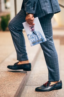 man in black long sleeve shirt and blue denim jeans holding a book