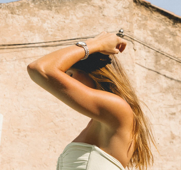 A woman in profile with her arm raised over her head, her face hidden by her arm and hair (raised-arm stand-in; the underarm itself is not shown)
