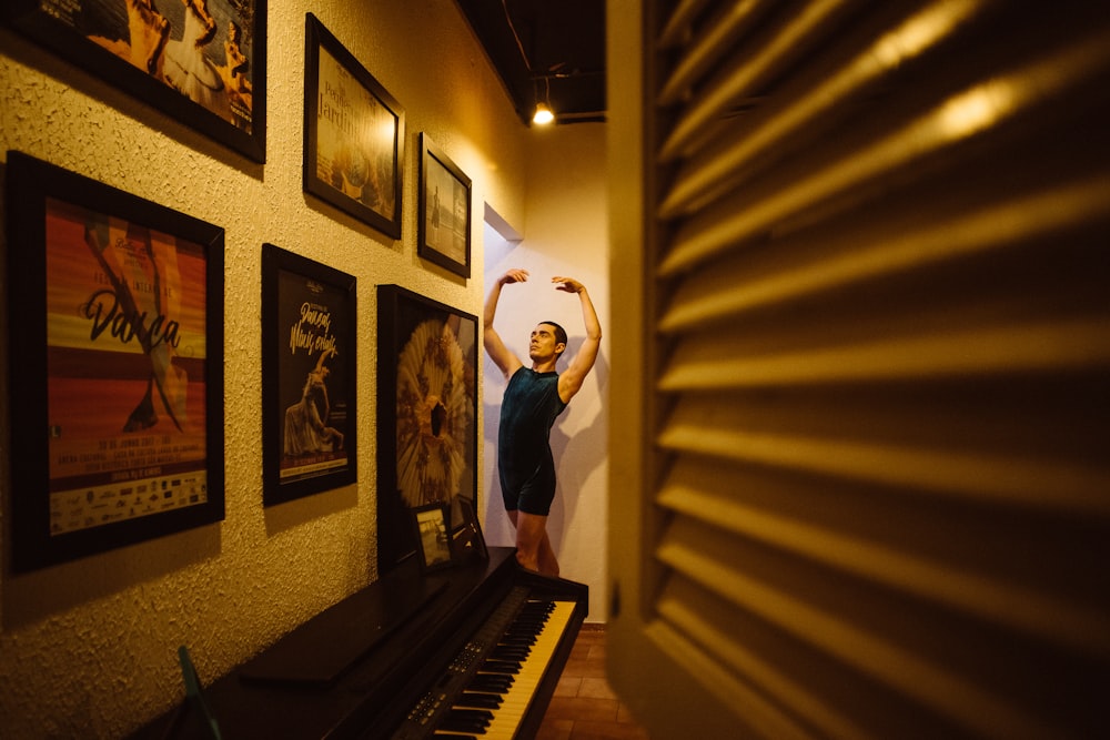 man in blue t-shirt and black pants standing beside brown wooden piano