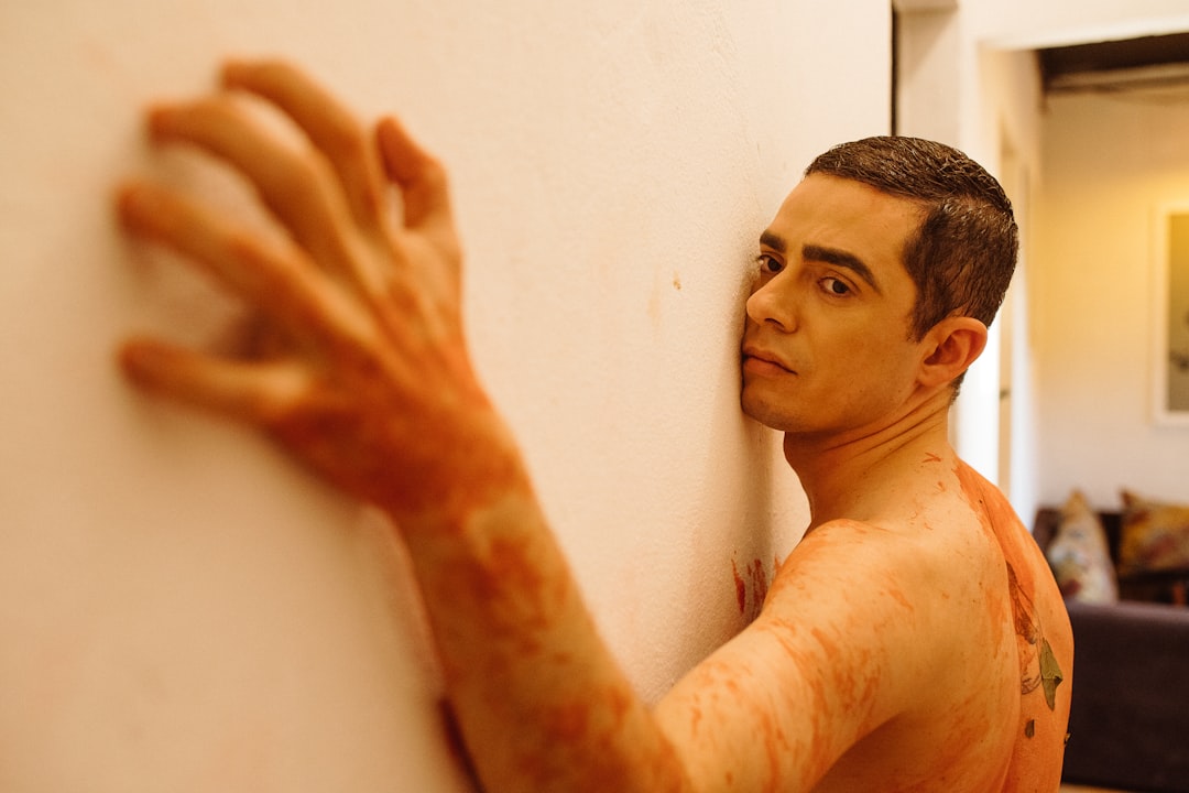 topless man leaning on white wall