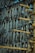 A close-up view of numerous fish hanging vertically on wooden racks, likely for the purpose of drying. The arrangement of the fish is dense and orderly, with each fish suspended head-down alongside others. The wooden racks are constructed of unrefined bamboo poles, tied together with rope, suggesting a traditional method of fish preservation. The background is partially visible, showing a clear blue sky.