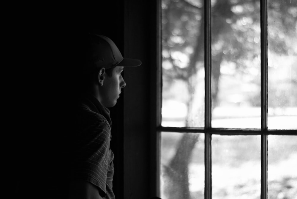 grayscale photo of man looking at the window