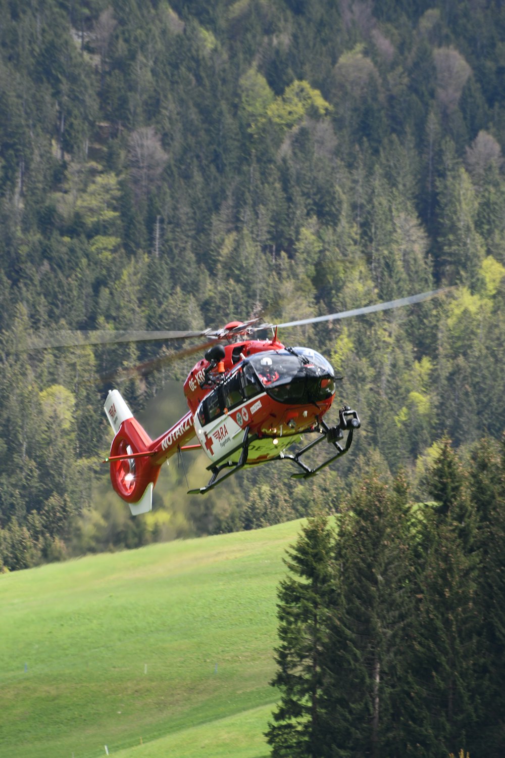 red and white helicopter flying over green grass field during daytime