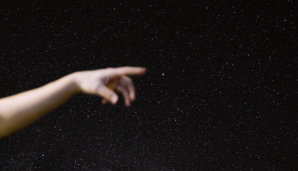 a hand reaching for the stars in the night sky