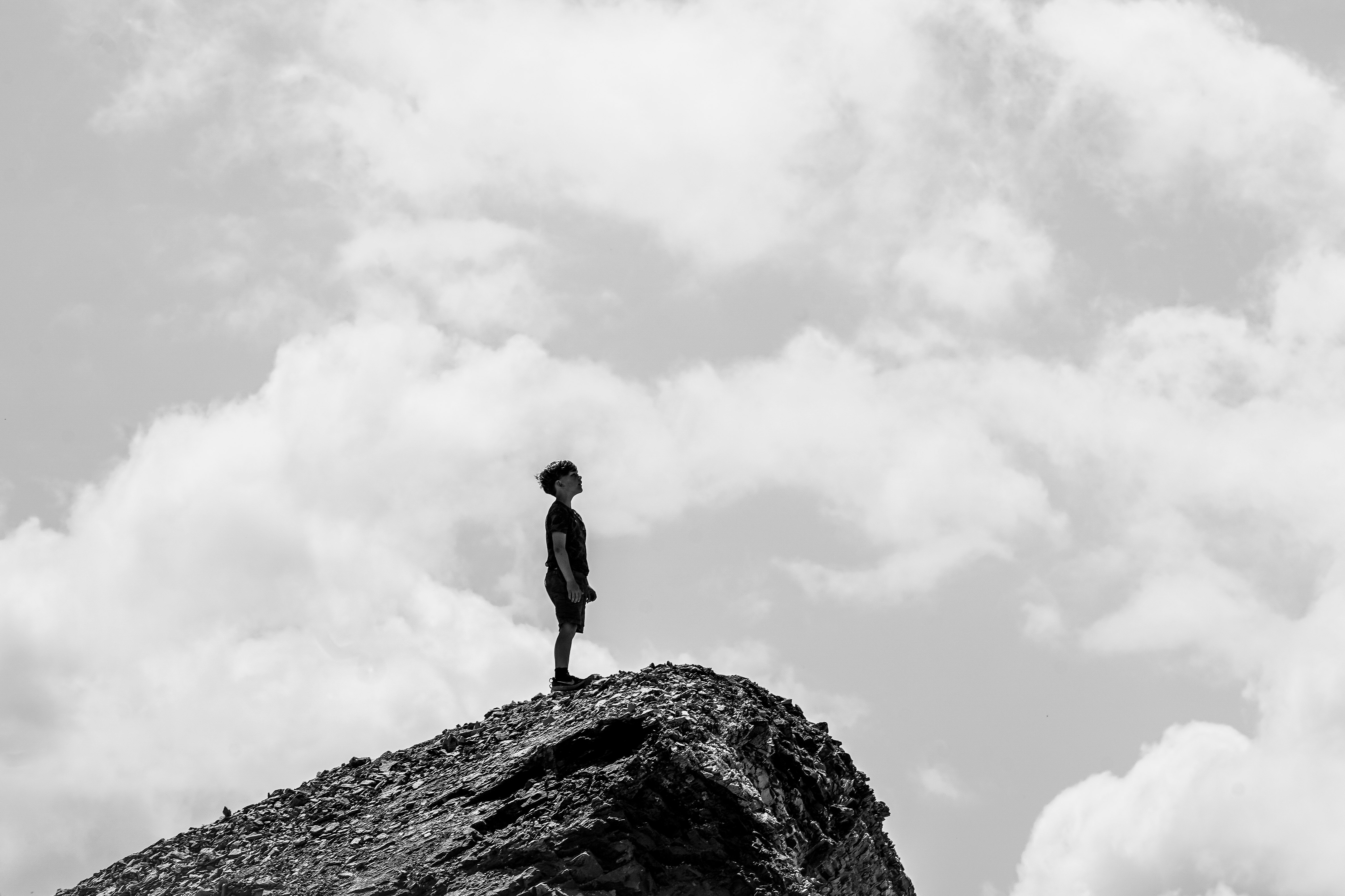 grayscale photo of man standing on rock formation