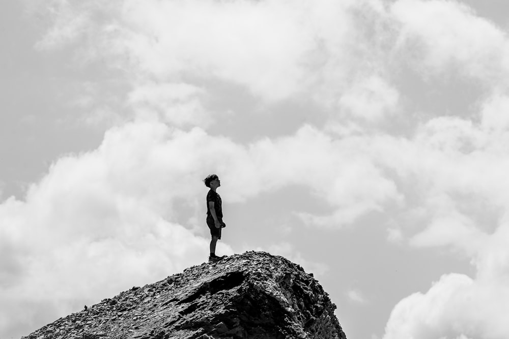 grayscale photo of man standing on rock formation