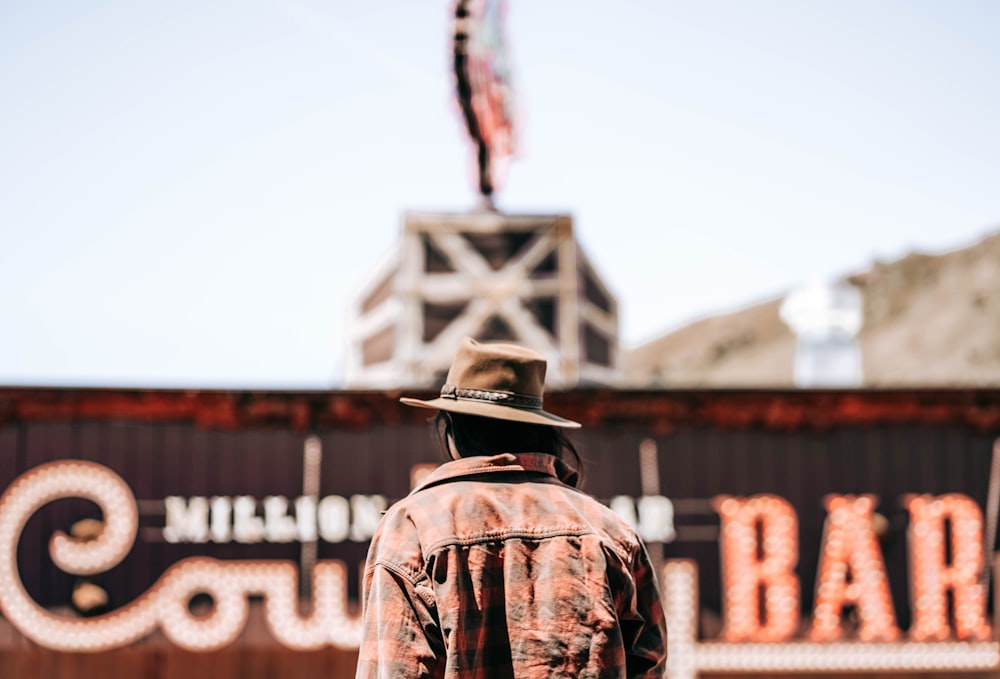 man in brown and black camouflage jacket wearing black hat standing near brown building during daytime