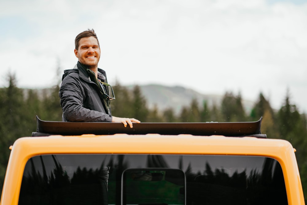 man in black jacket sitting on yellow and black car during daytime