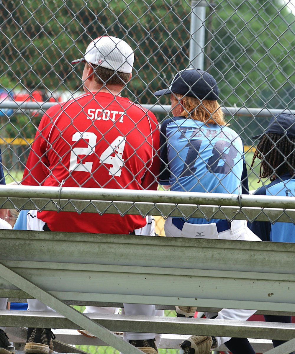 man in red and white baseball jersey shirt sitting on white bench during daytime