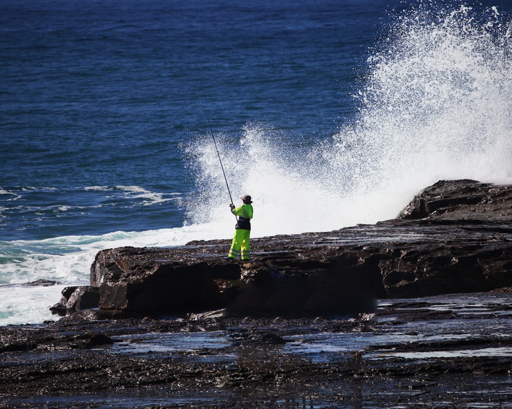 Hombre con camisa verde y pantalones verdes de pie en la roca cerca del mar durante el día