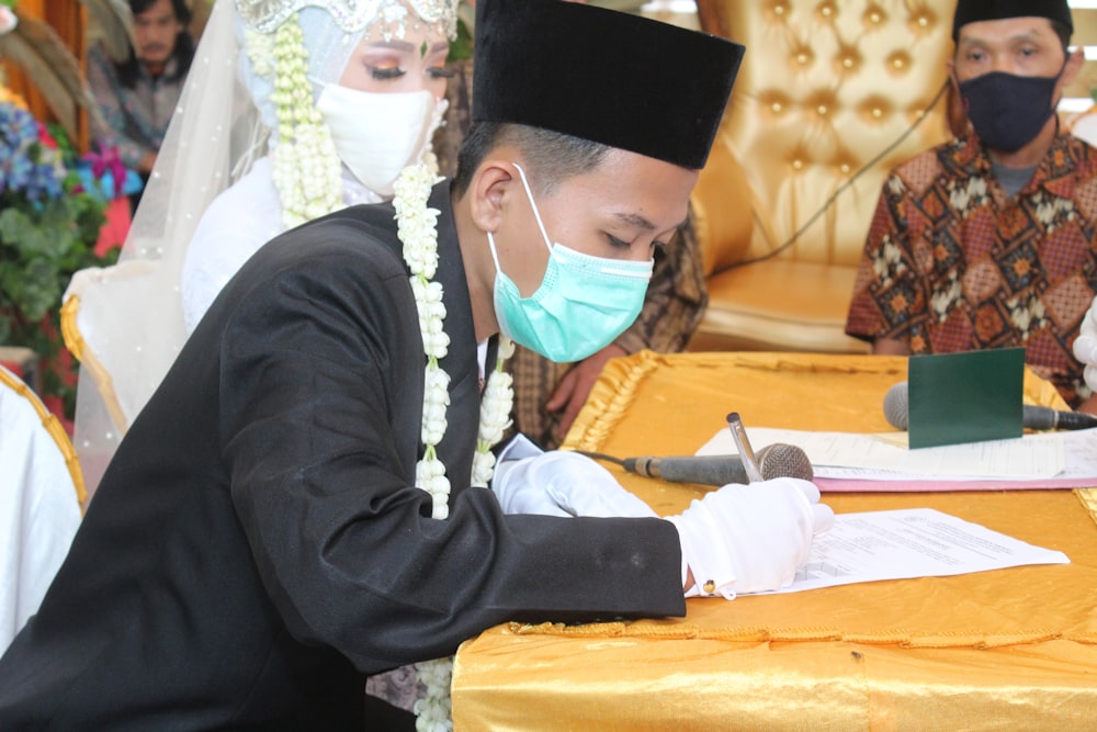 man in black academic dress and white hijab sitting on chair