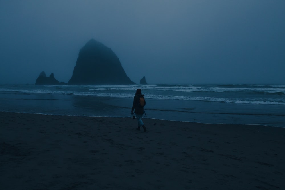 donna in camicia nera che cammina sulla spiaggia durante il giorno