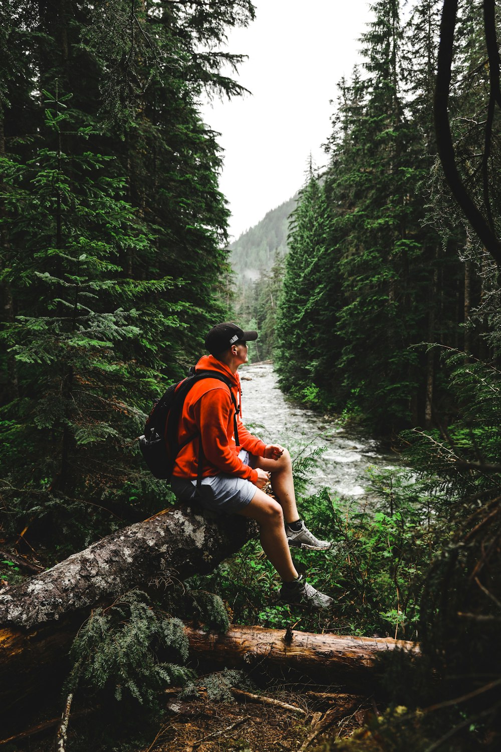 man in orange shirt and blue denim shorts sitting on rock in the middle of forest