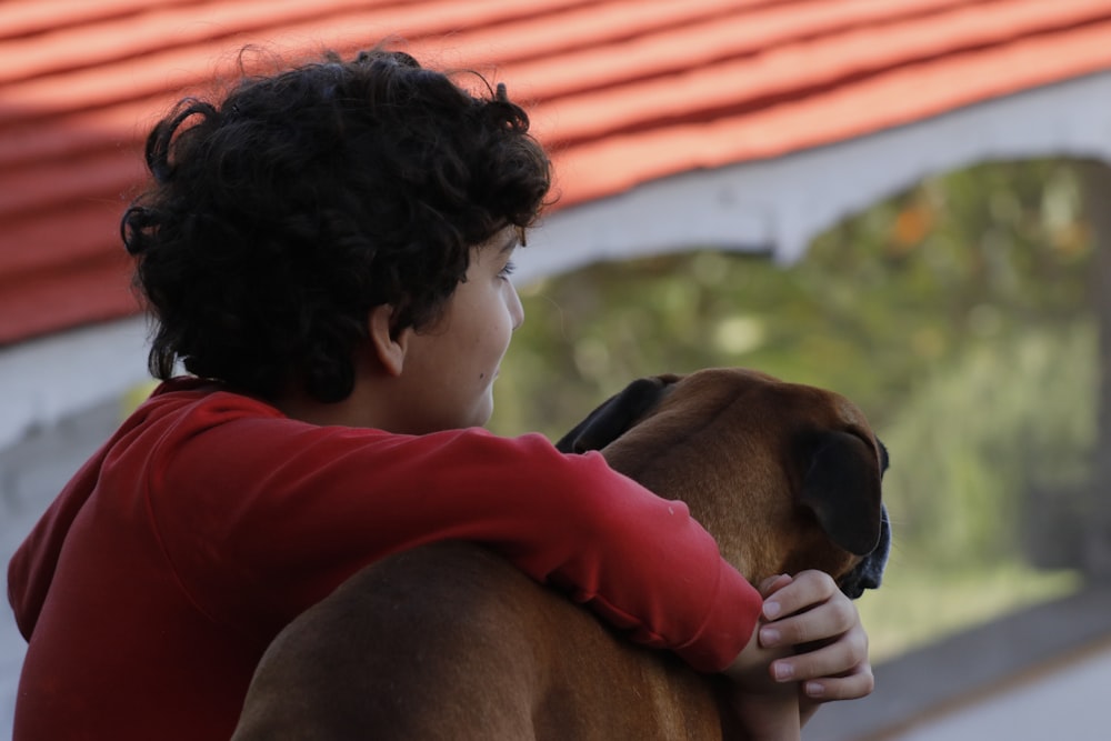 boy in red shirt kissing brown short coated dog