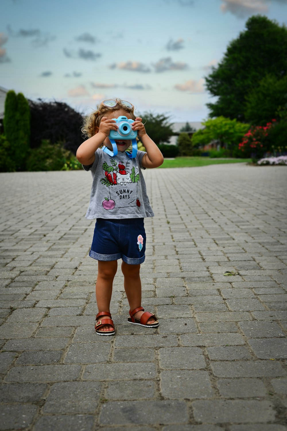 girl in white and pink floral shirt and blue denim shorts standing on gray concrete pathway