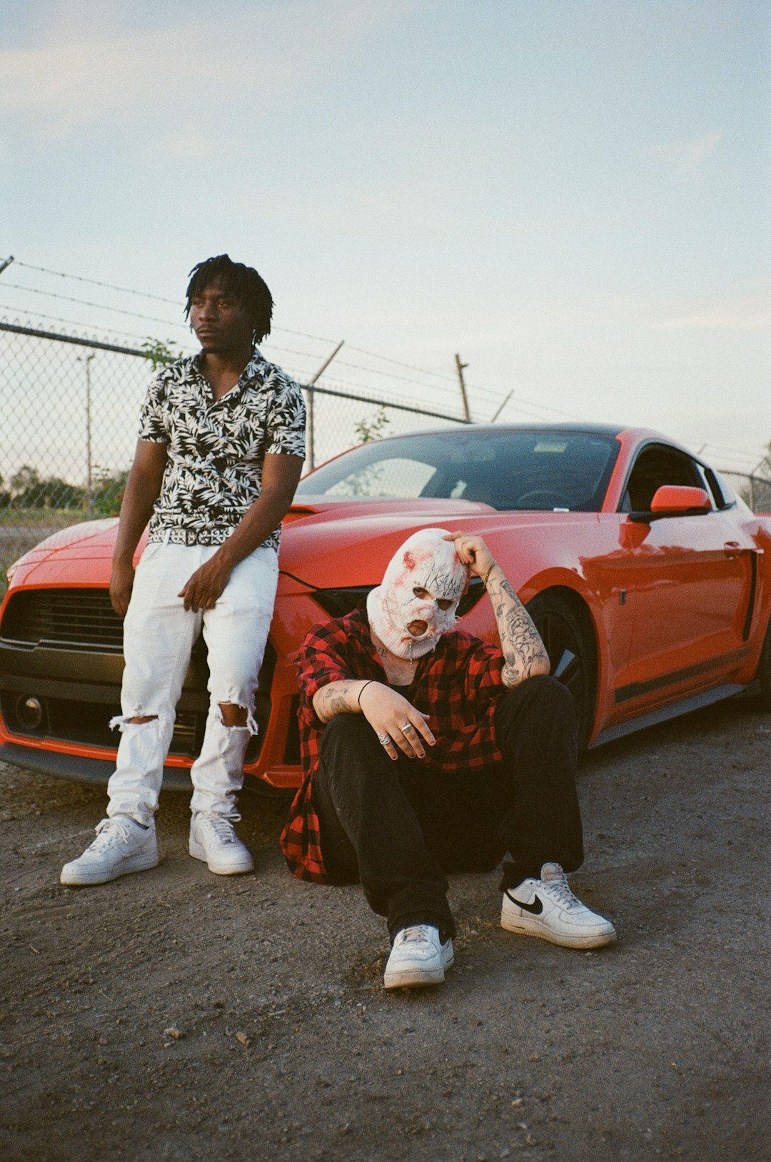 woman in black and white floral shirt and white pants sitting on red car