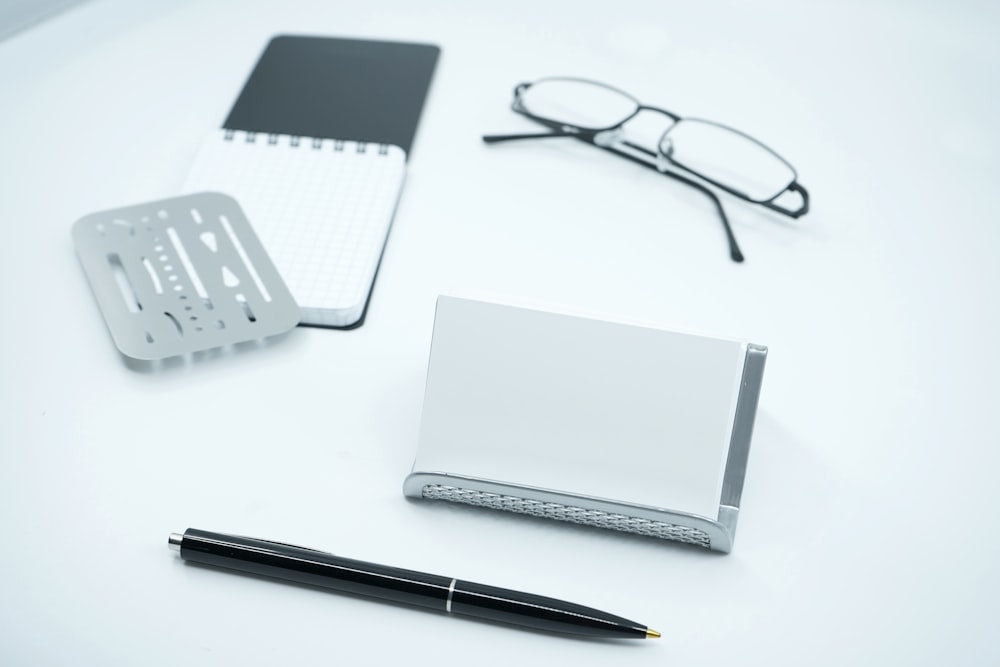 black framed eyeglasses beside white printer paper and black pen