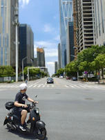 A rider wearing a helmet cruising through an urban street with skyscrapers in the background.