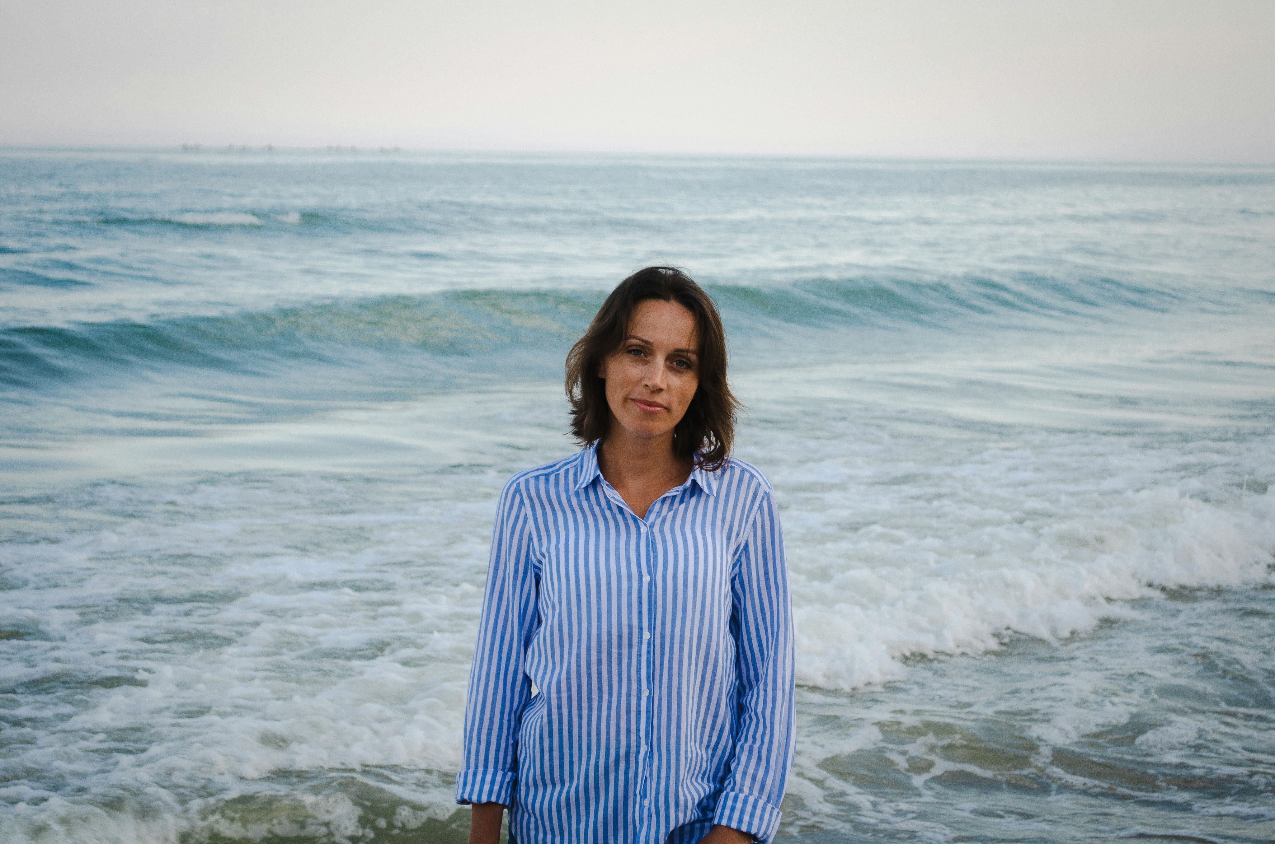 woman in blue and white striped dress shirt standing on beach during daytime