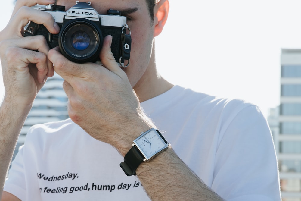 man in white shirt holding black nikon dslr camera