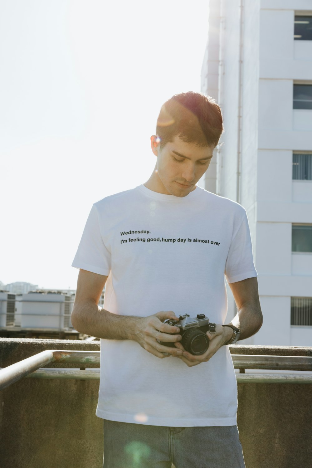 Hombre con camiseta blanca de cuello redondo sosteniendo una cámara DSLR negra