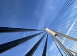 Cables stretch upwards, converging at the top of a bridge pylon against a clear blue sky, showcasing the architectural design and engineering.
