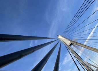 Cables stretch upwards, converging at the top of a bridge pylon against a clear blue sky, showcasing the architectural design and engineering.
