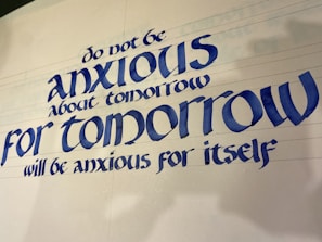 A piece of calligraphy featuring a motivational quote written in elegant, bold blue letters. The text provides reassurance about the future, suggesting not to worry about tomorrow.