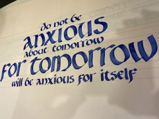 A piece of calligraphy featuring a motivational quote written in elegant, bold blue letters. The text provides reassurance about the future, suggesting not to worry about tomorrow.