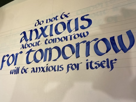 A piece of calligraphy featuring a motivational quote written in elegant, bold blue letters. The text provides reassurance about the future, suggesting not to worry about tomorrow.