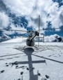 black and gray helicopter flying over snow covered ground under blue and white cloudy sky during