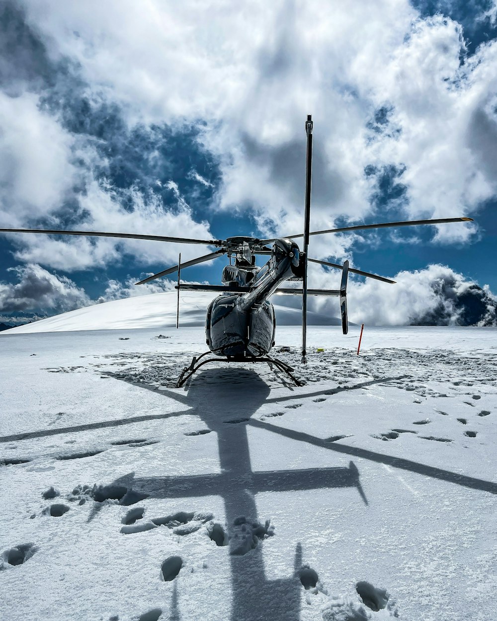 black and gray helicopter flying over snow covered ground under blue and white cloudy sky during