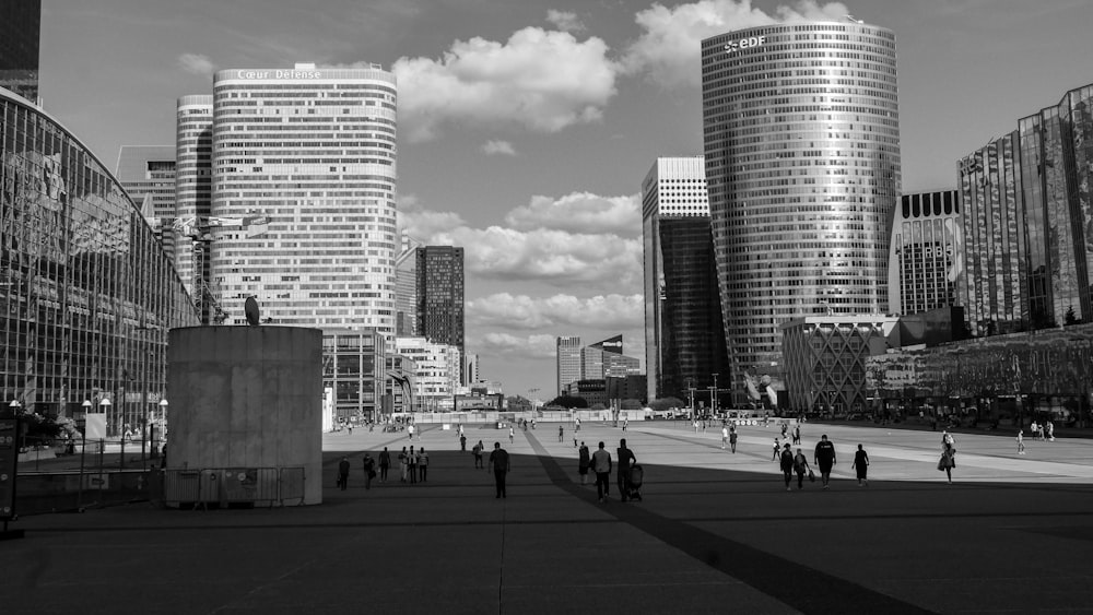 grayscale photo of people walking on street near high rise buildings