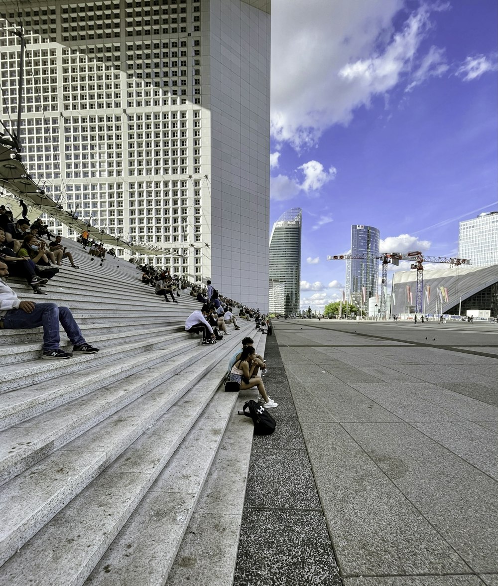 people sitting on gray concrete pavement near high rise buildings during daytime