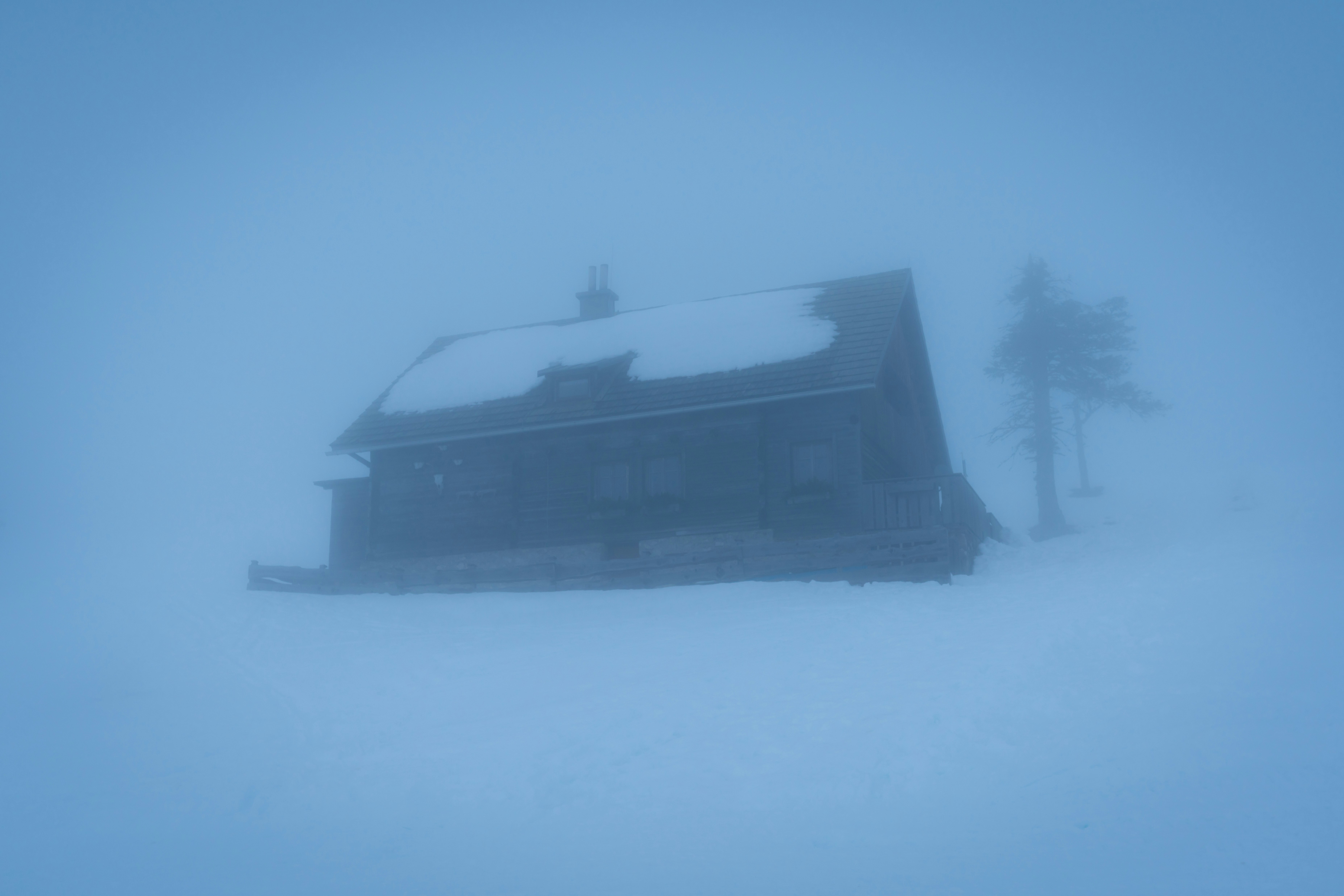 black and white house on snow covered ground, Creepy cabin in thick fog during a whiteout at blue hour in Dobratsch Natural Park, Villach, Carinthia, Austria