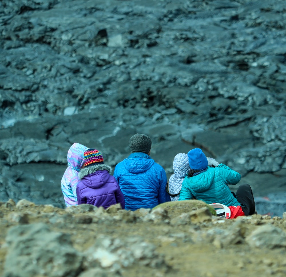 3 Kinder sitzen tagsüber auf braunem Felsen