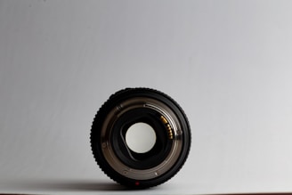 A sleek camera lens resting on a clean white surface, capturing natural light reflections.