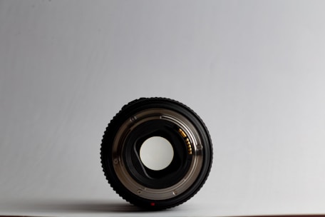 A sleek camera lens resting on a clean white surface, capturing natural light reflections.