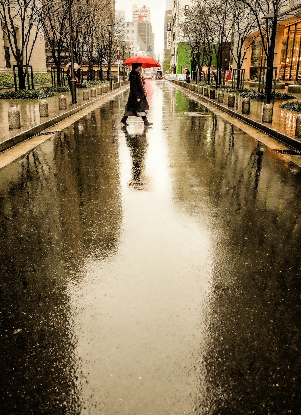 person in red jacket walking on wet road during daytime