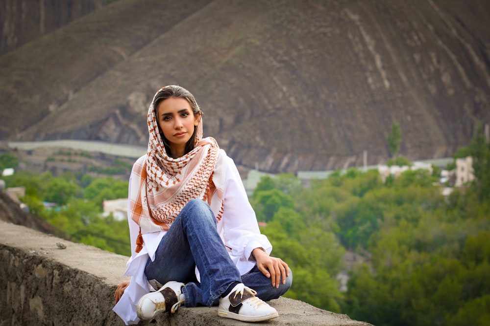 woman in white long sleeve shirt and blue denim jeans sitting on rock