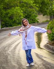 woman in white long sleeve shirt and blue denim jeans standing on gray asphalt road during