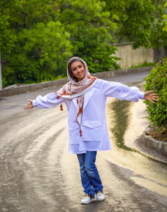 woman in white long sleeve shirt and blue denim jeans standing on gray asphalt road during