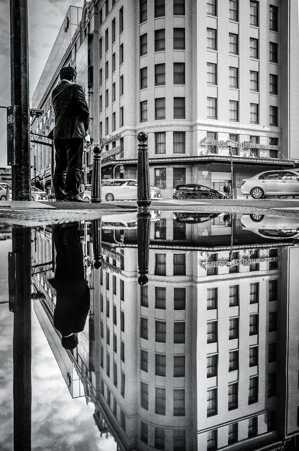 grayscale photo of man in black jacket and pants standing on bridge