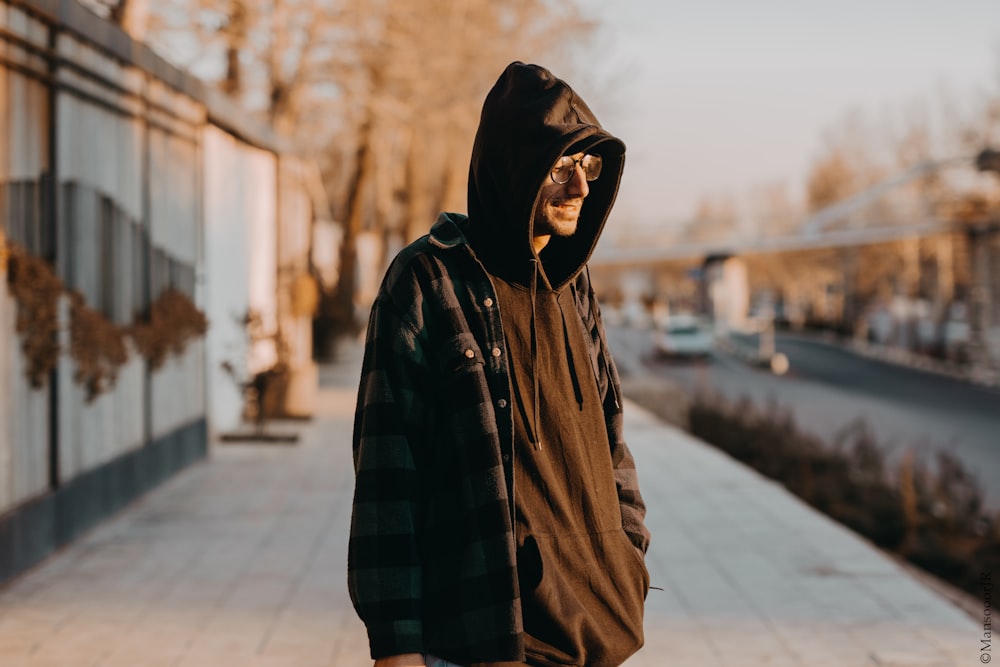 man in black and brown plaid hoodie standing on sidewalk during daytime