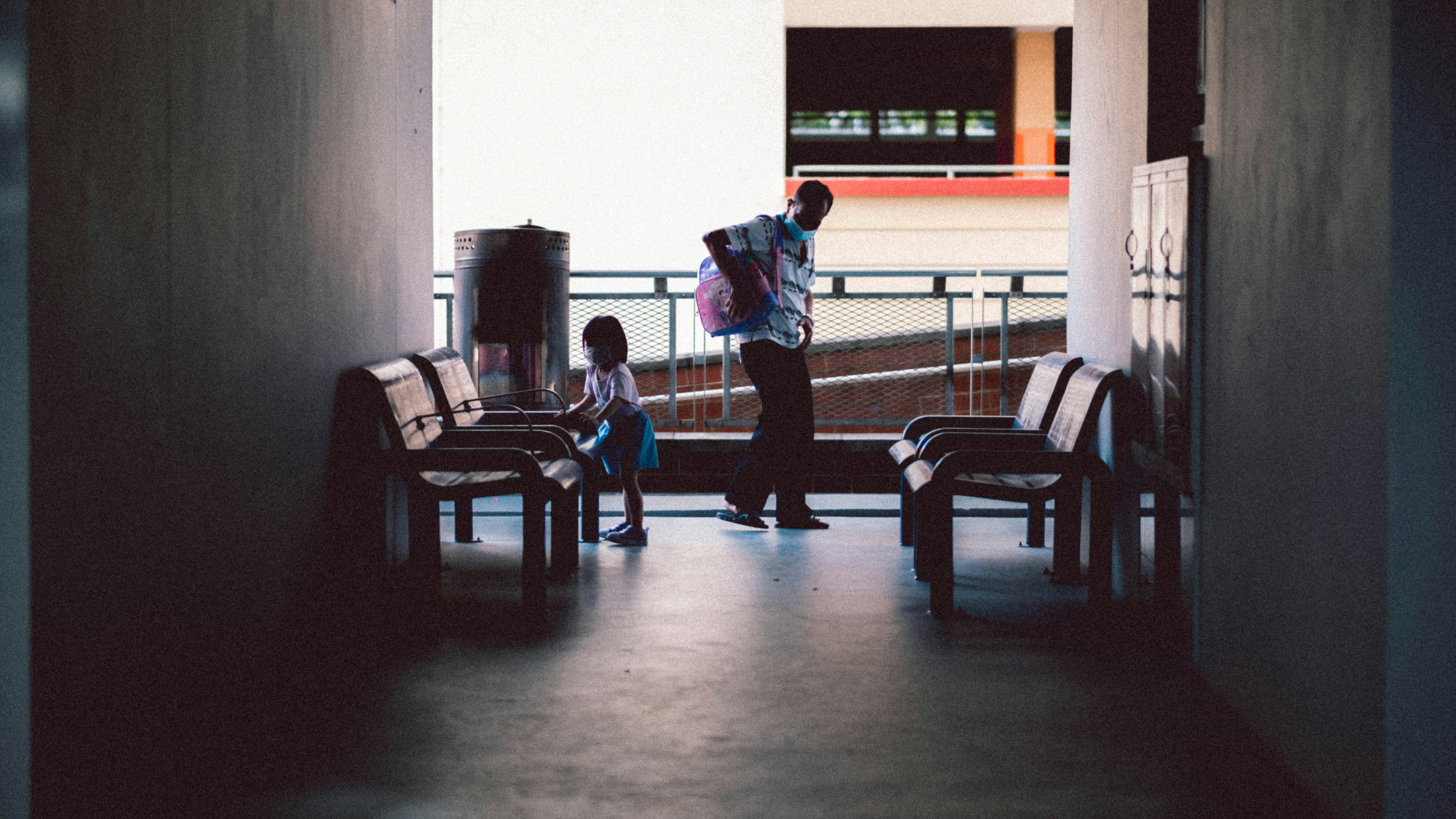 boy in blue shirt and black pants standing near brown wooden armchair