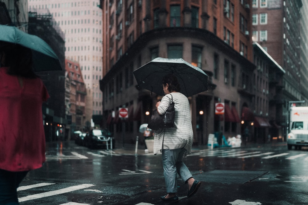 woman in gray jacket and black pants holding umbrella walking on street during daytime