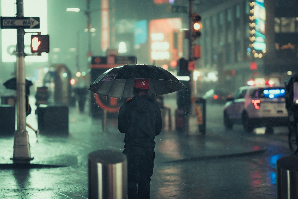 man in black jacket holding umbrella walking on street during night time